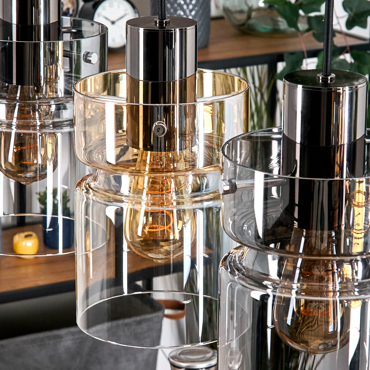 Nahaufnahme von drei modernen Pendelleuchten. Jede hat ein metallisches Oberteil und einen Glasschirm mit einer sichtbaren Glühbirne.