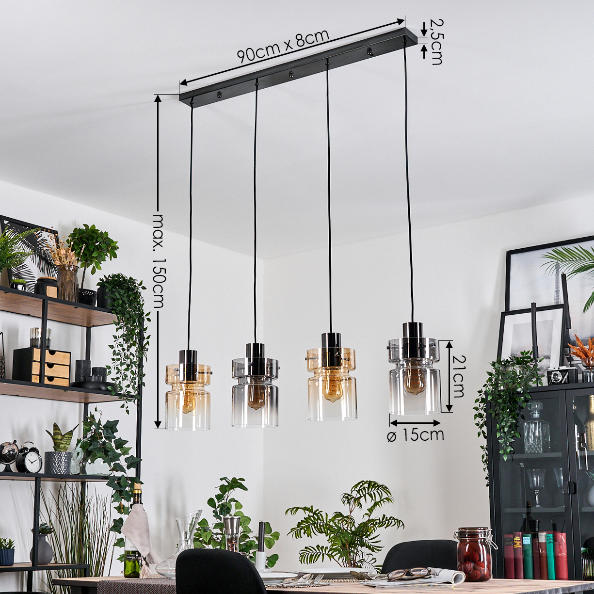 Vierflammige Pendelleuchte mit schwarzem Rahmen. Klare und bernsteinfarbene Glasschirme. Maße sind 90x8cm und max. 150cm Fall. Pflanzen und Möbel im Hintergrund.