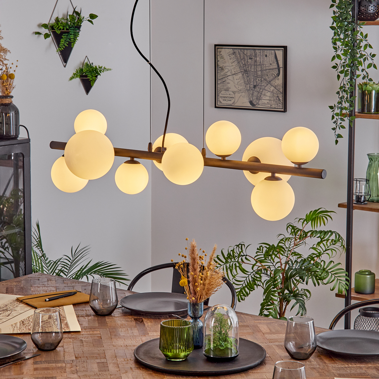Ein Esszimmer mit einem Holztisch, der zum Abendessen gedeckt ist. Eine moderne Deckenleuchte hängt darüber. Pflanzen und Dekoration sind sichtbar.