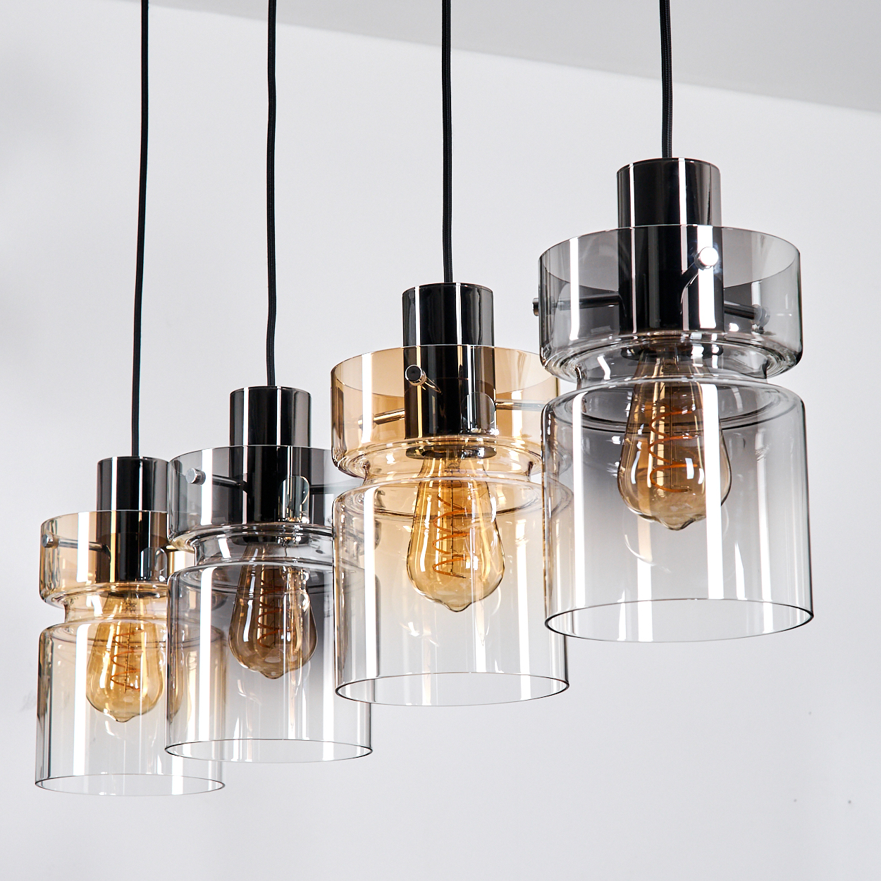 Vier moderne Pendelleuchten mit Glasschirmen und freiliegenden Edison-Glühbirnen hängen vor weißem Hintergrund.