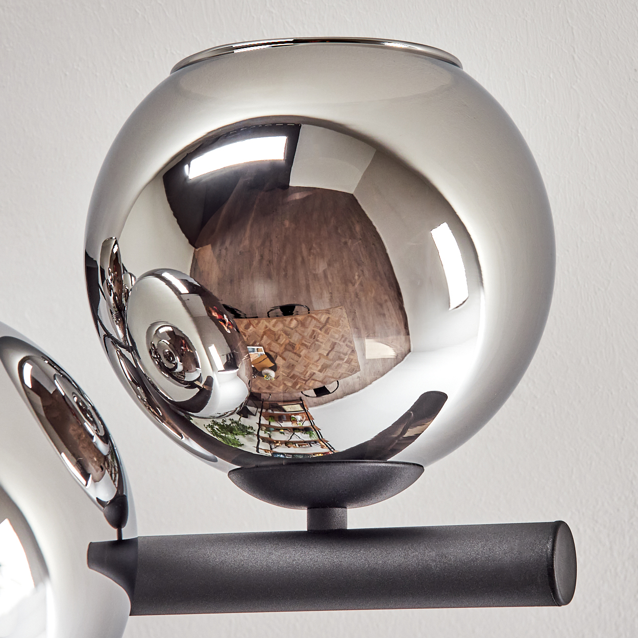 Moderne Lampe mit verchromten Kugeln, die einen Raum reflektieren. Ein schwarzer Arm hält die Kugeln. Der Hintergrund ist eine weiße Wand.