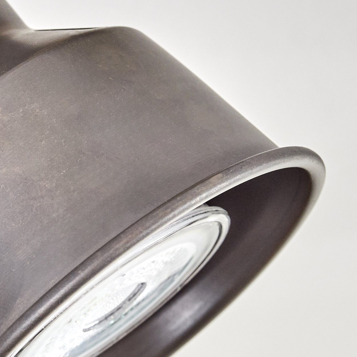 Nahaufnahme eines dunklen Metall-Lampenschirms mit Glaskolben. Der Hintergrund ist schlicht weiß.