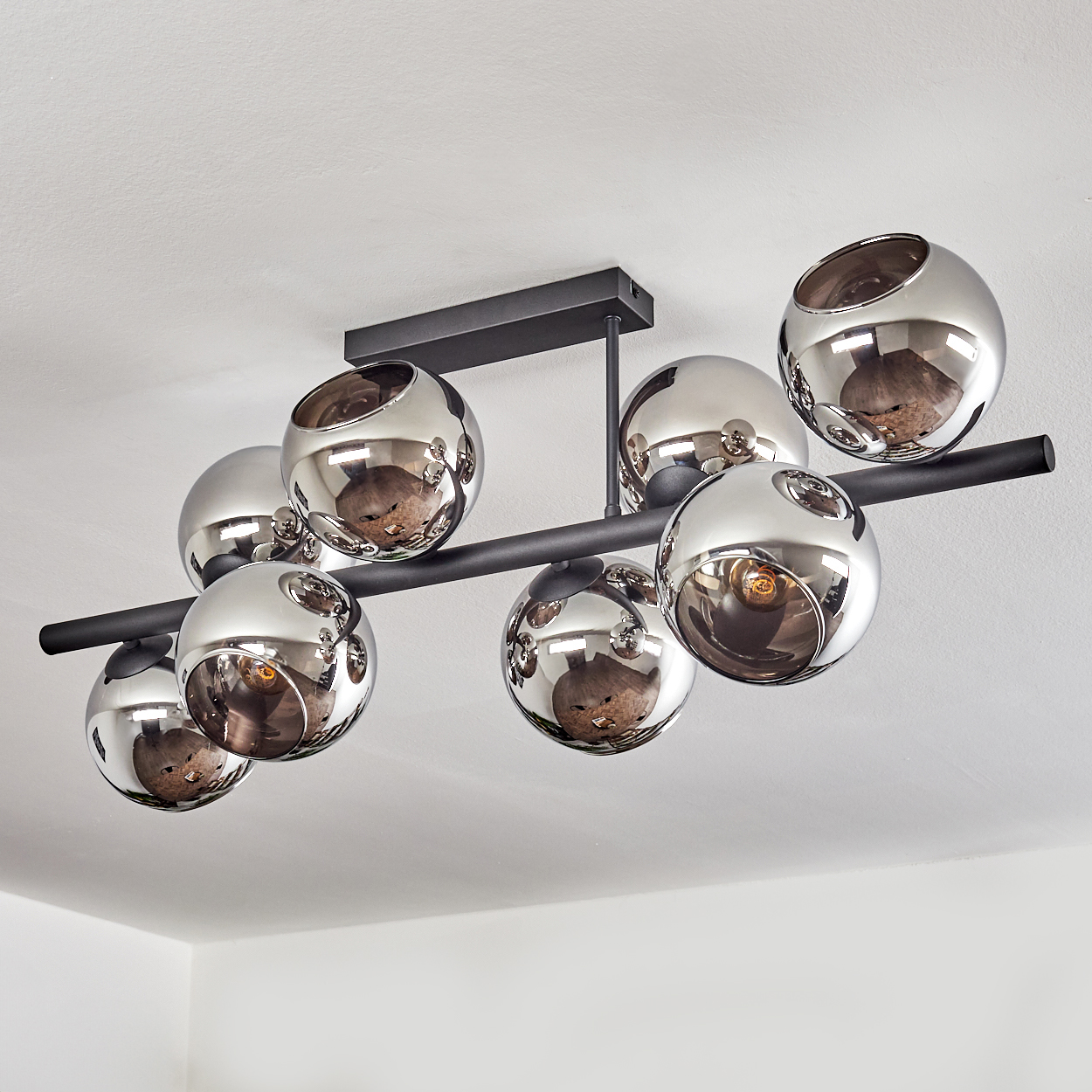 Moderne Deckenleuchte mit verchromten Kugeln. Sie hat eine schwarze rechteckige Basis und horizontale Stangen.