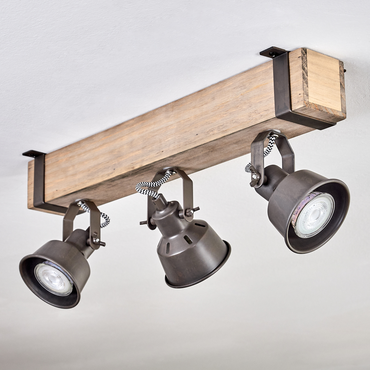 Drei Strahler an einem Holzbalken befestigt. Die Leuchten sind aus dunklem Metall mit sichtbaren Glühbirnen. Schwarz-weiß gestreifte Kordeln werden verwendet.