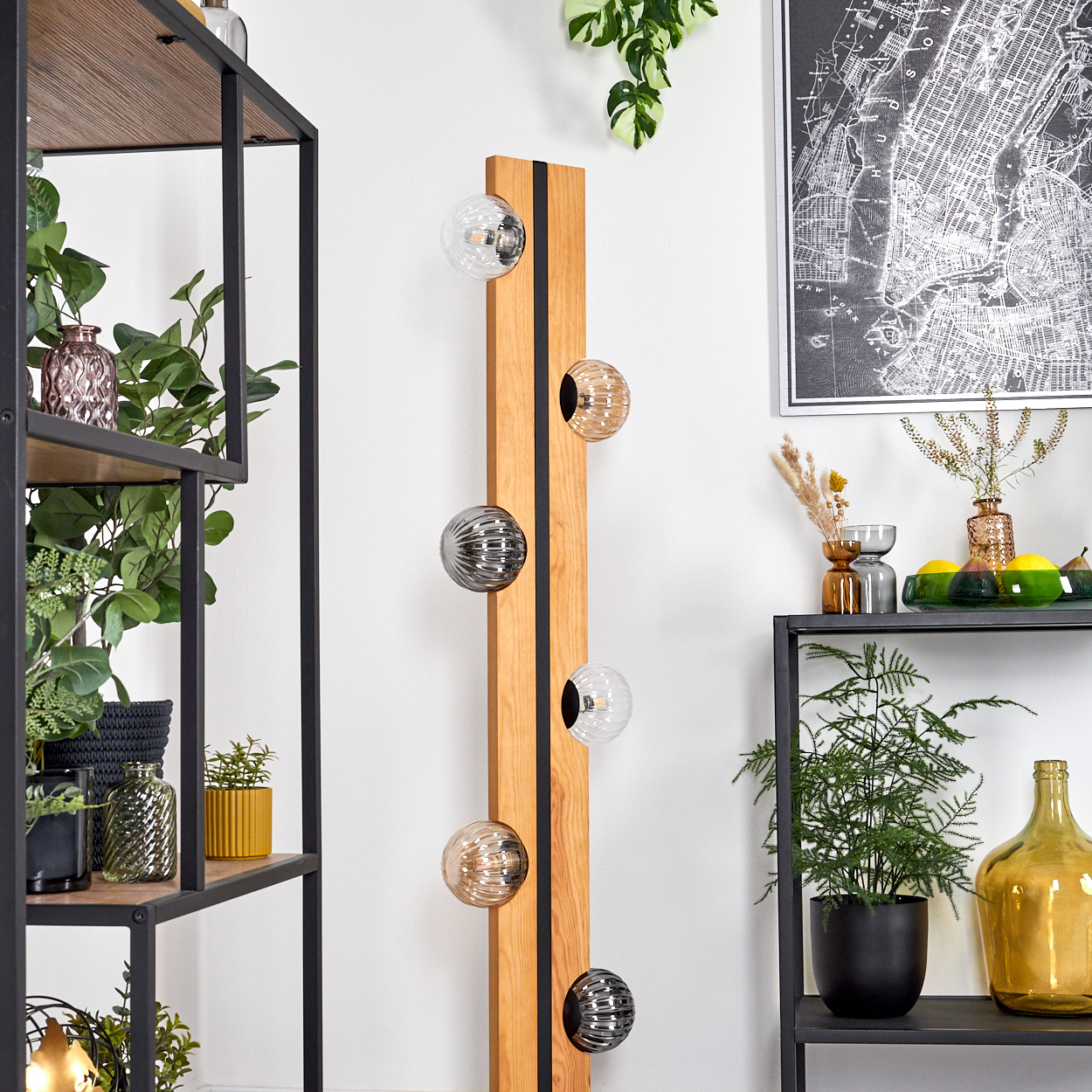 Eine Holzlampe mit Kugelleuchten steht neben Regalen mit Pflanzen und Dekoration. An der Wand hängt eine Karte.