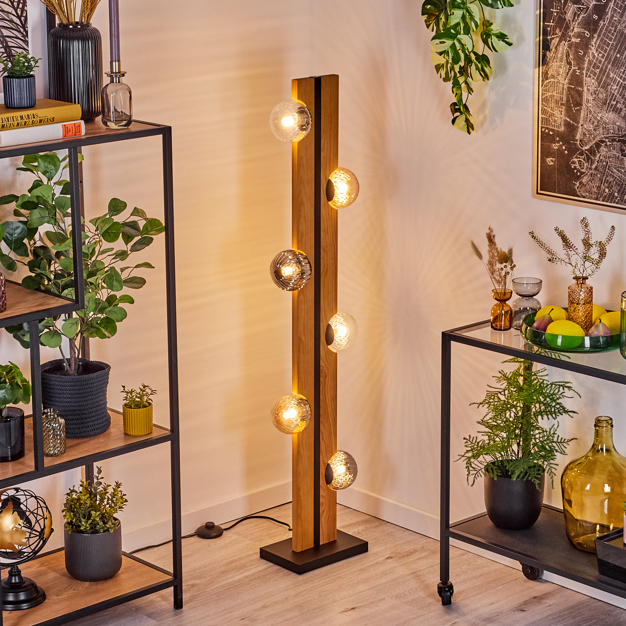 Eine moderne Stehlampe mit Glaskugelleuchten steht neben Regalen mit Pflanzen und Dekoration. Der Hintergrund umfasst Kunstwerke und weitere Pflanzen.