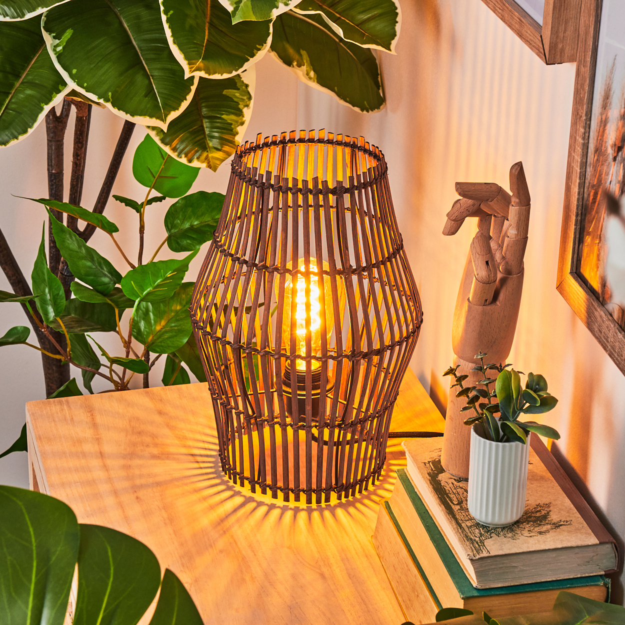 Eine beleuchtete Lampe mit Holzrahmen steht auf einem Holztisch. Pflanzen und eine Holzhandskulptur befinden sich in der Nähe.