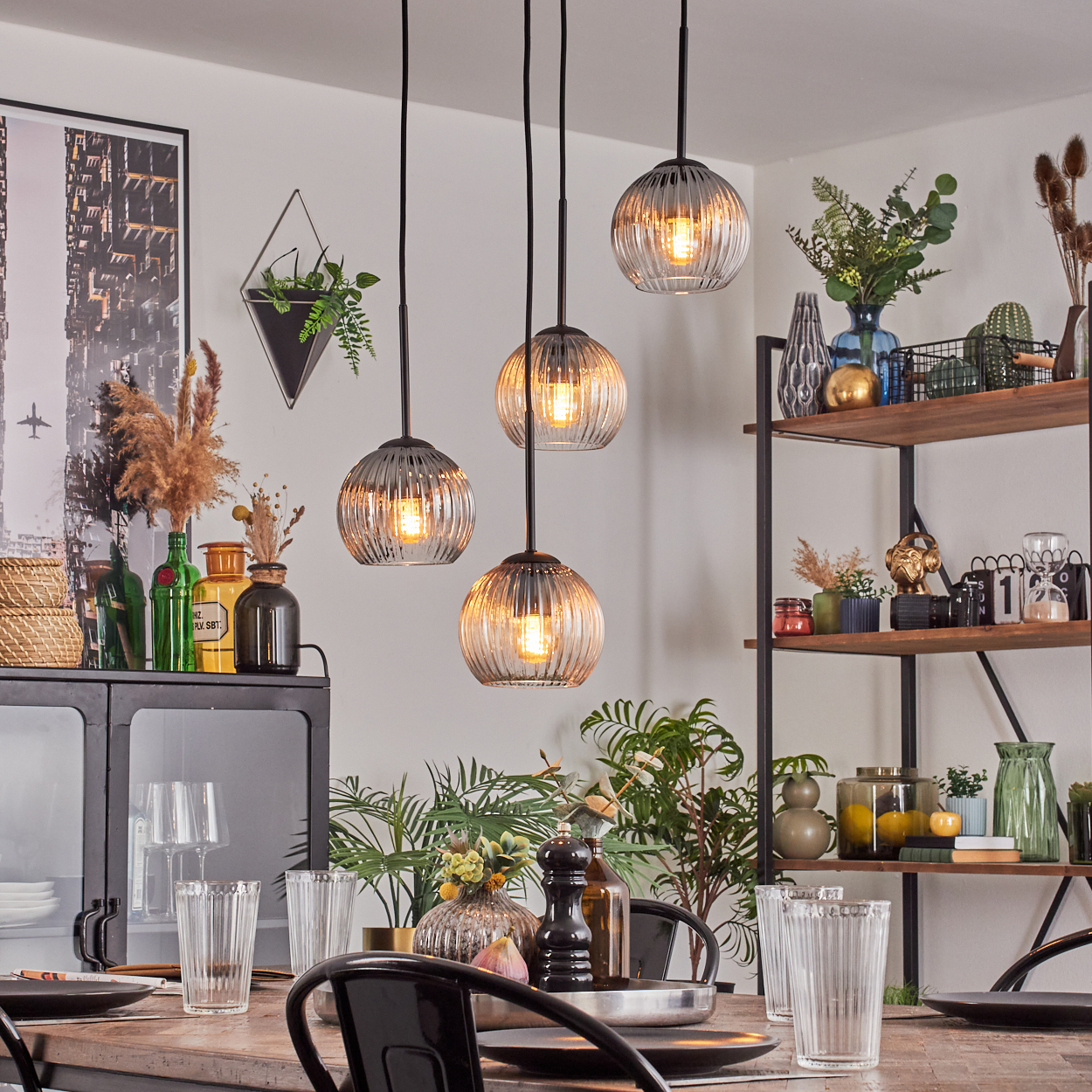 Esszimmer mit Hängelampen, Tisch, Regalen mit Pflanzen und Dekor. Fokus auf die Lampen und den Esstisch.