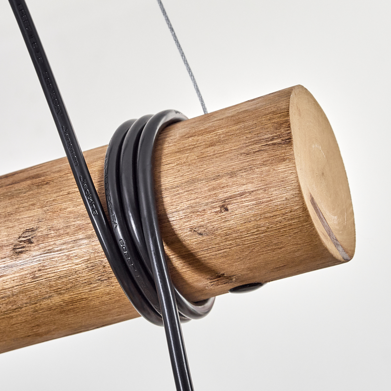 Nahaufnahme eines Holzbalkens mit schwarzen Kabeln. Ein Metallkabel hält den Balken vor weißem Hintergrund.