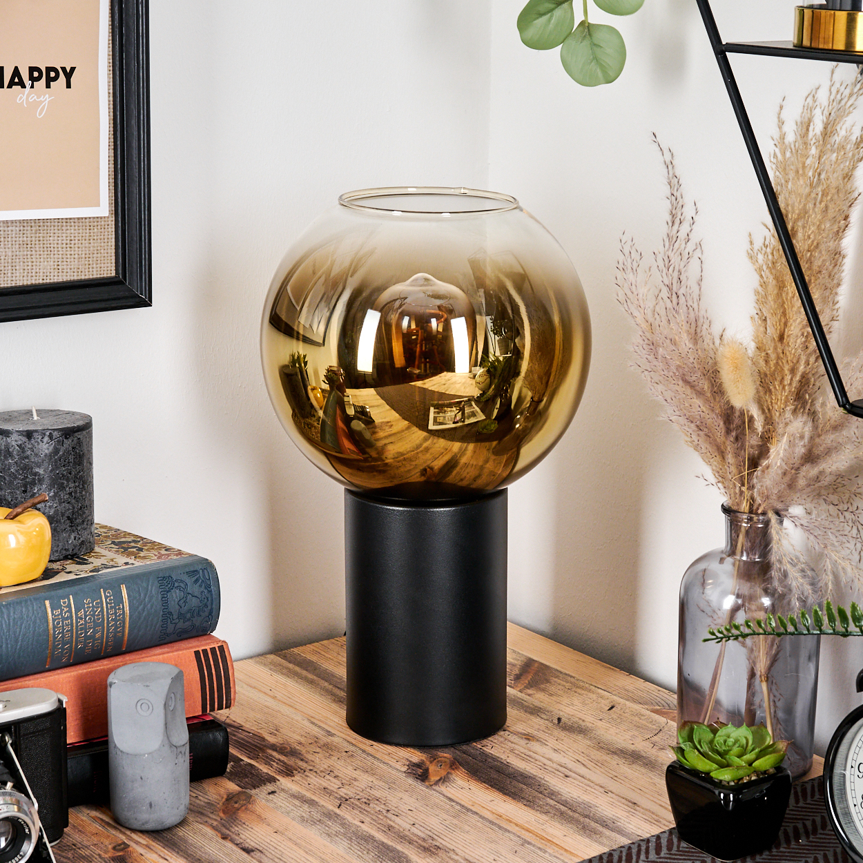 Eine goldene Glaskugel steht auf einem schwarzen Sockel. Bücher, eine Kerze und eine Kamera liegen auf Holz.
