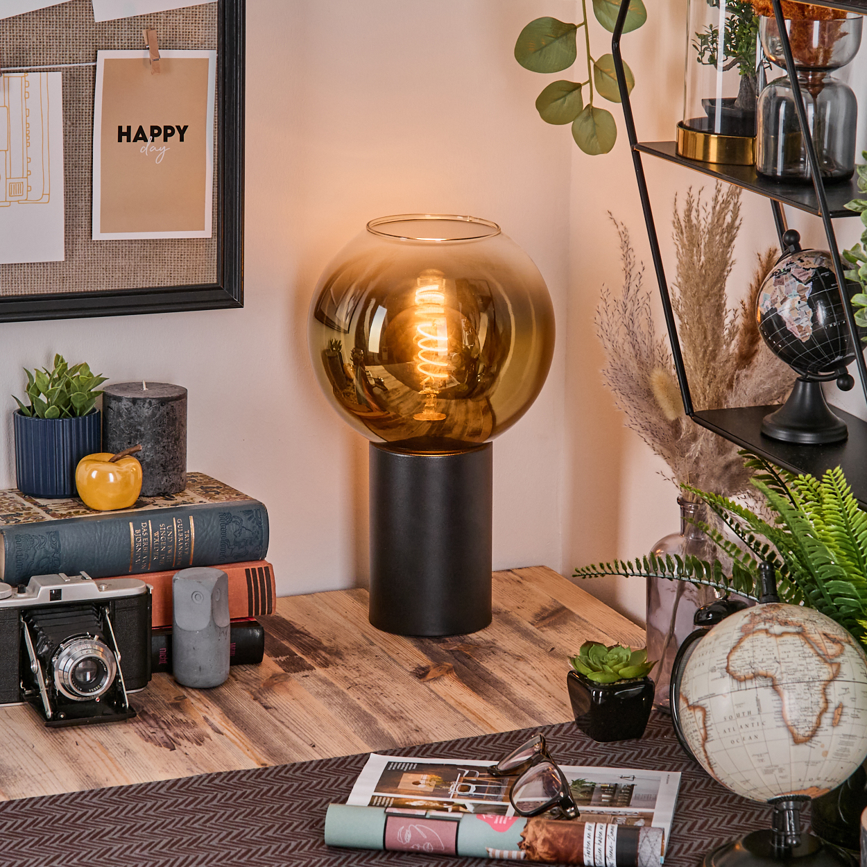 Ein Schreibtisch mit Lampe, Büchern, Kamera, Globus und Pflanzen. Die Lampe ist das zentrale Element.