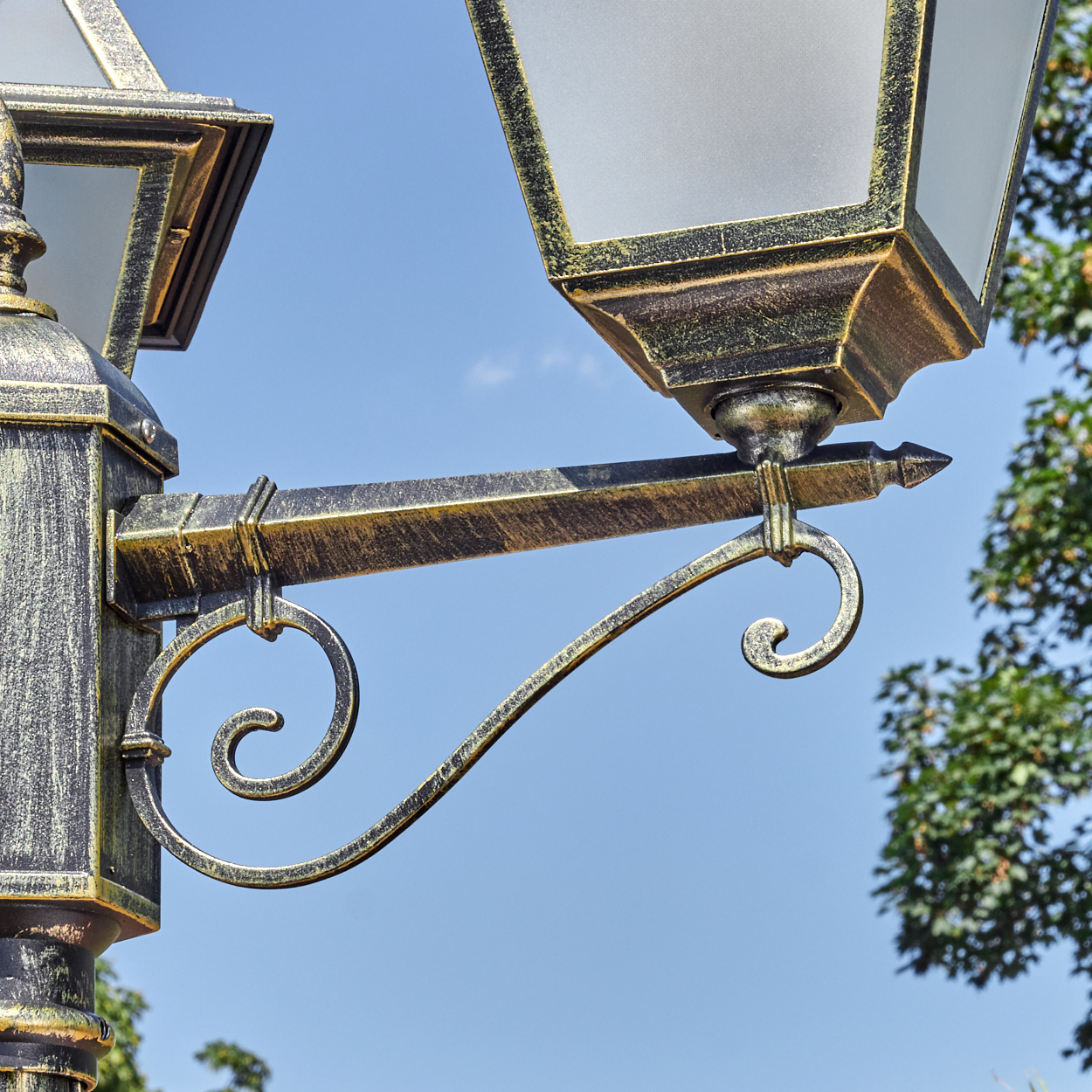 Nahaufnahme einer dekorativen Laterne. Die Lampe ist schwarz und gold mit einer Milchglasscheibe. Blauer Himmel im Hintergrund.