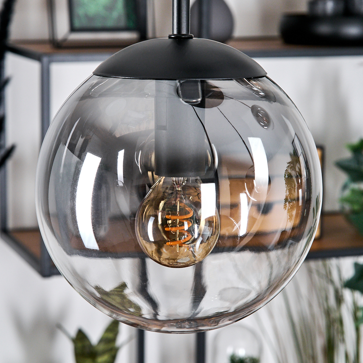 Nahaufnahme einer modernen, kugelförmigen Pendelleuchte mit klarem Glasschirm und sichtbarer, warmtoniger Glühbirne.