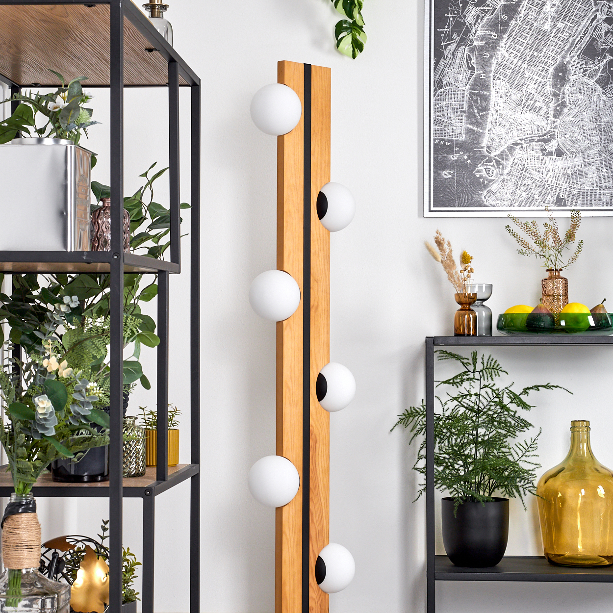 Holzlampe mit weißen Kugeln, schwarze Regale mit Pflanzen und Dekoration, eine Karte und eine Glasflasche.
