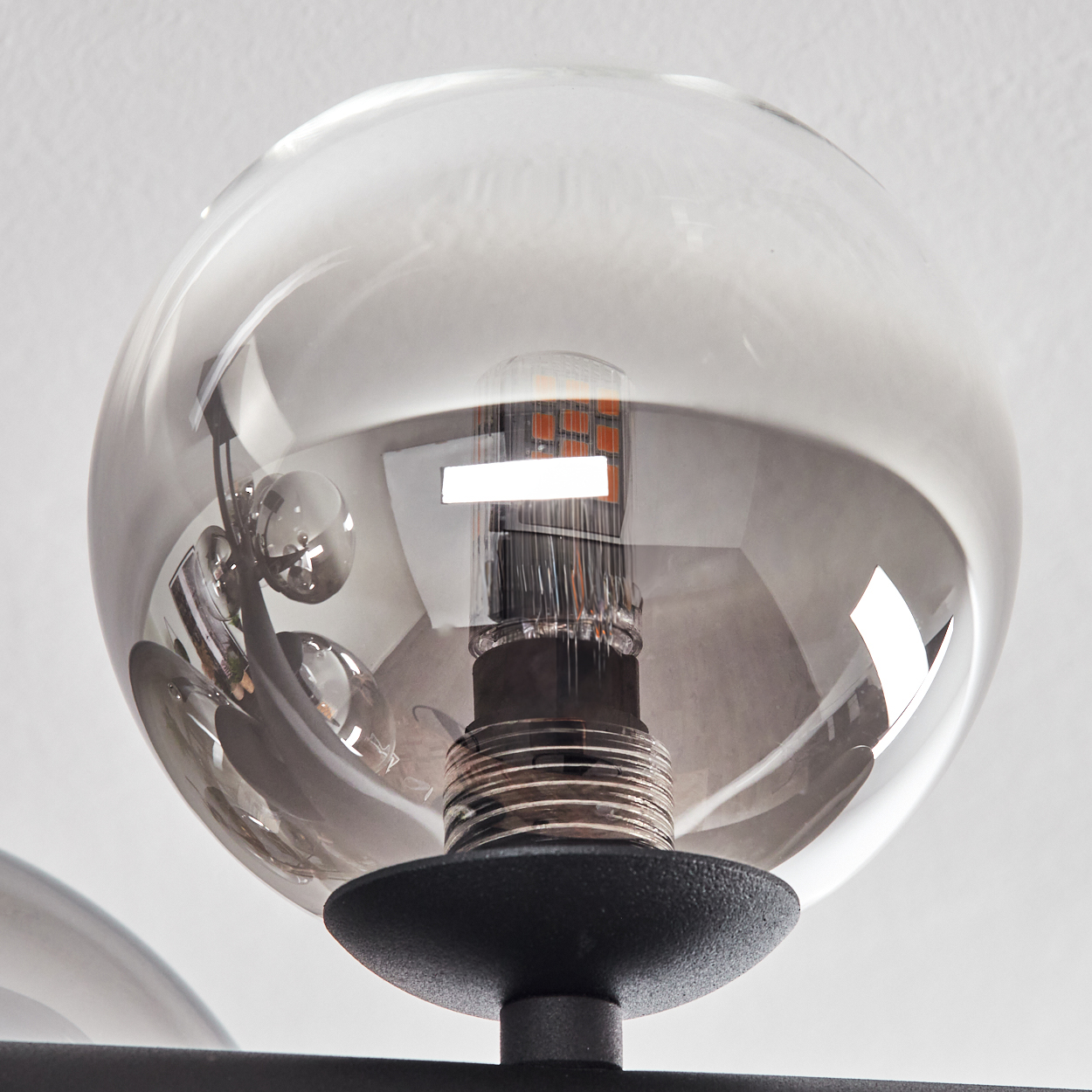 Nahaufnahme einer modernen Leuchte. Eine klare Glaskugel umschließt eine Glühbirne. Schwarzer Metallsockel. Weißer Hintergrund.