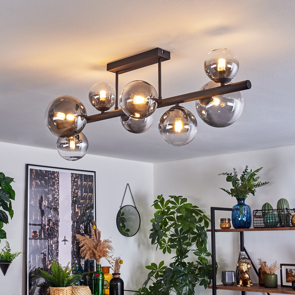 Eine moderne Deckenleuchte mit kugelförmigen Glaskolben. Pflanzen und Dekorationen sind im Raum. Ein Bild an der Wand und ein Spiegel.