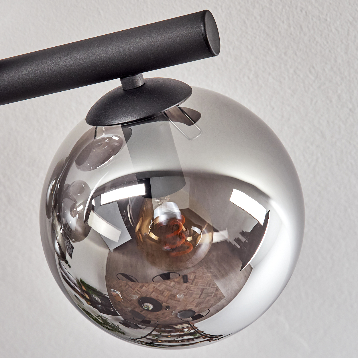Eine moderne Lampe mit schwarzem Arm und einem reflektierenden, kugelförmigen Glasschirm. Die Reflexion zeigt einen Raum mit Holzboden.