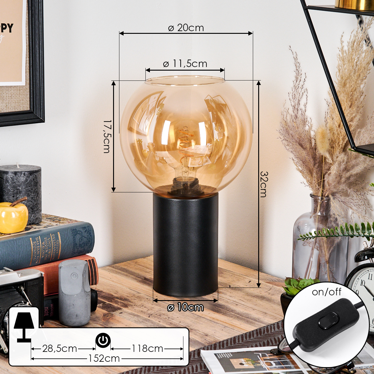 Eine moderne Lampe mit einem kugelförmigen, bernsteinfarbenen Glasschirm steht auf einem schwarzen, zylindrischen Sockel. Die Lampe steht auf einer Holzoberfläche mit anderen Dekorationen.