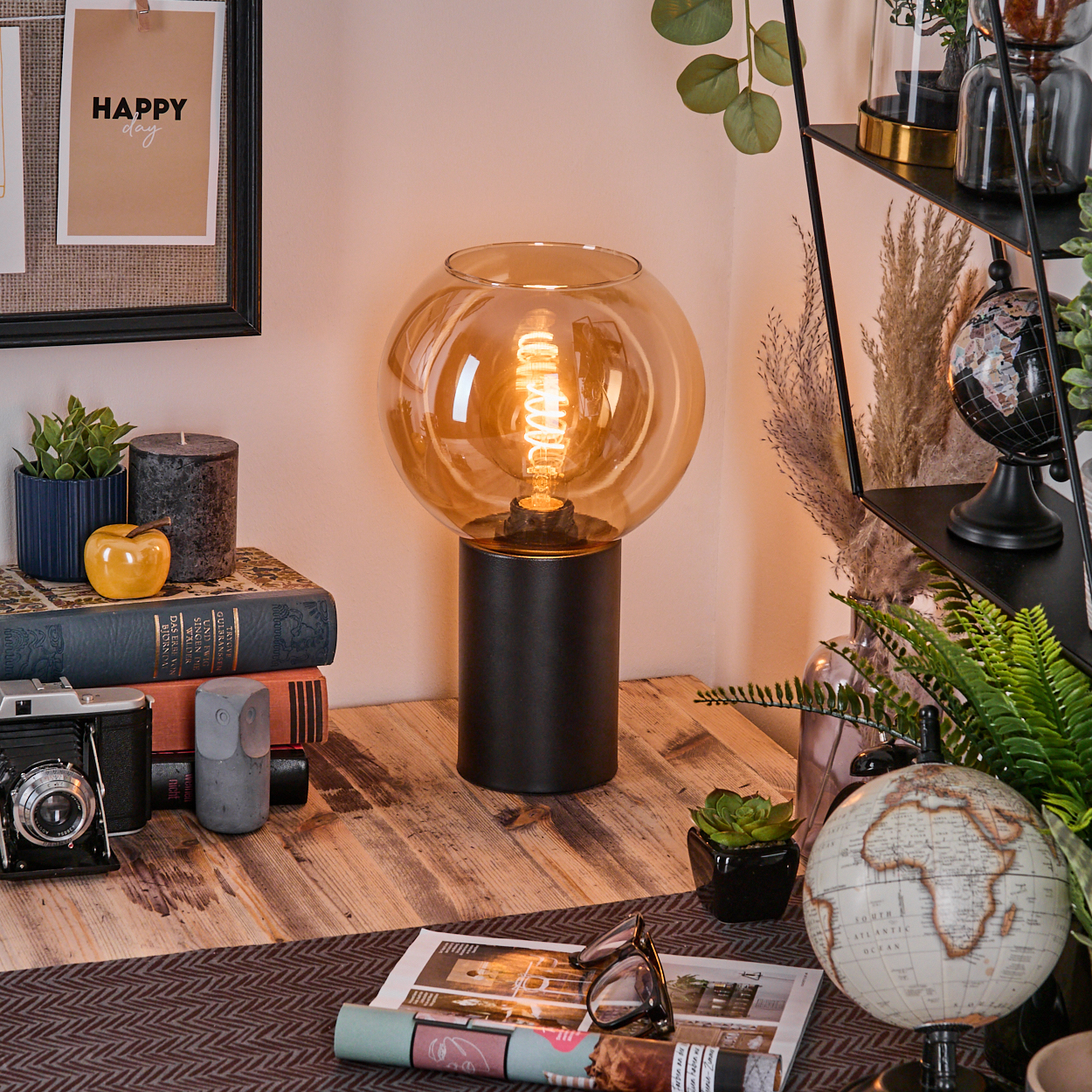 Ein Schreibtisch mit Lampe, Büchern, Kamera und Globus. Ein Schild sagt 'Happy day'. Regale mit Pflanzen und einem Globus sind im Hintergrund.