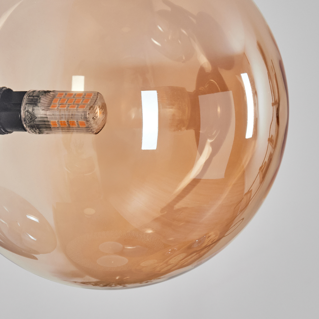 Nahaufnahme einer braunen Glasglühbirne mit schwarzem Sockel und einer orangefarbenen LED-Leuchte. Der Hintergrund ist weiß.
