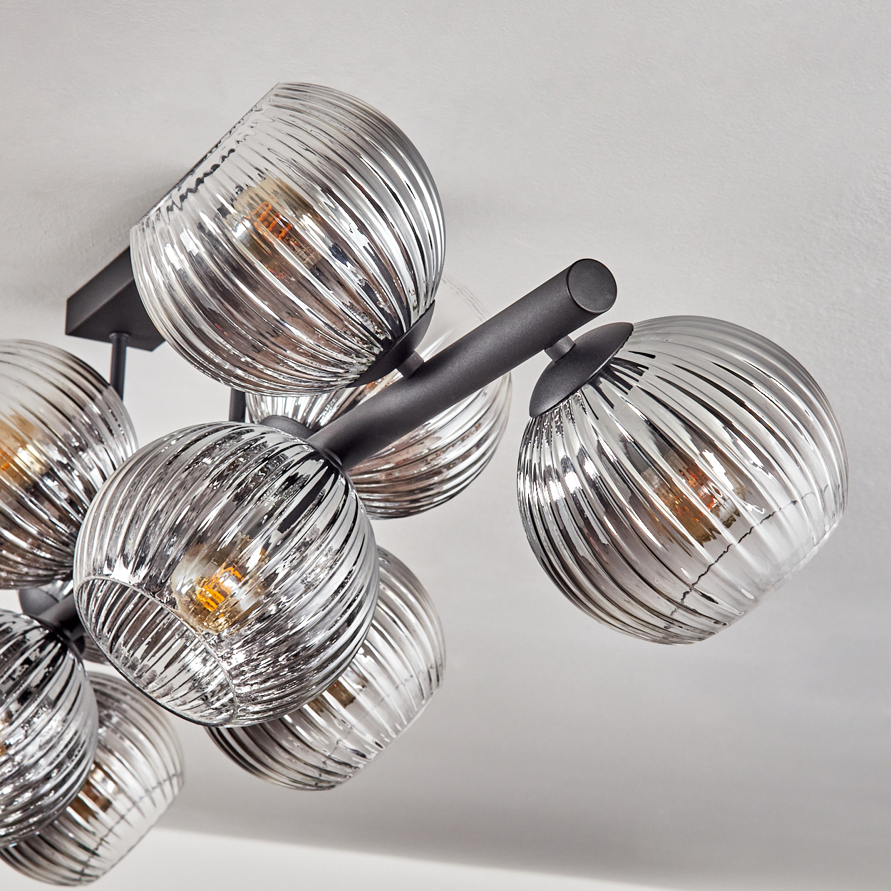Deckenlampe mit mehreren Glaskugeln. Die Kugeln sind geriffelt und silbern, mit warmen Glühbirnen im Inneren. Schwarze Arme stützen sie.