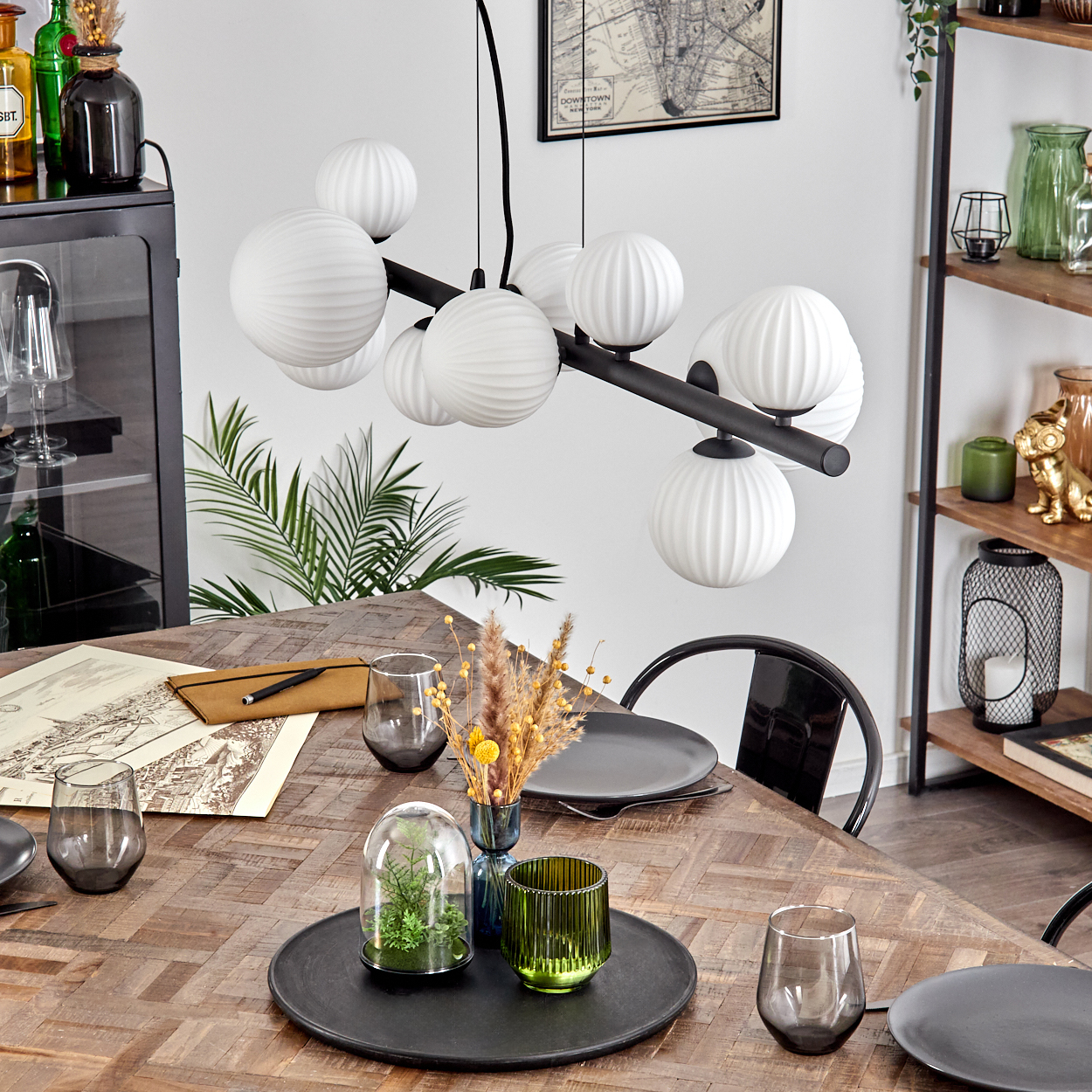 Esszimmer mit Holztisch, Glaskuppel, Gläsern, Kronleuchter, schwarzem Stuhl und Karte an der Wand.