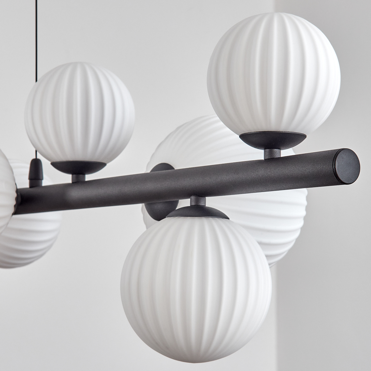 Eine moderne Deckenleuchte mit mehreren weißen, kugelförmigen Lampen mit gerippter Textur, die an einer dunklen horizontalen Stange befestigt sind.