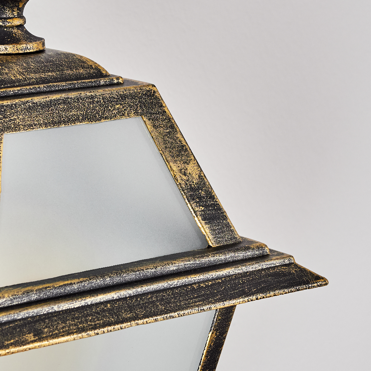 Nahaufnahme einer dekorativen Lampe mit einem schwarz-goldenen Rahmen und Milchglasscheiben vor weißem Hintergrund.