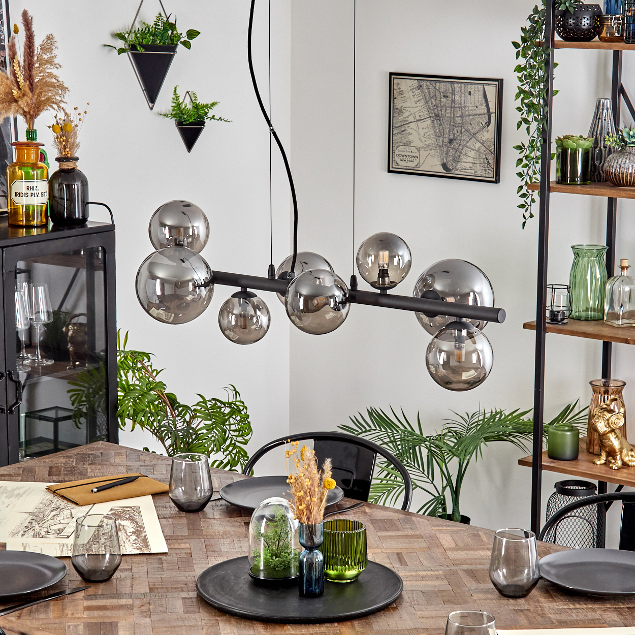 Ein Esszimmer mit Holztisch, modernem Kronleuchter und Dekoartikeln. Pflanzen und Gläser stehen auf dem Tisch.