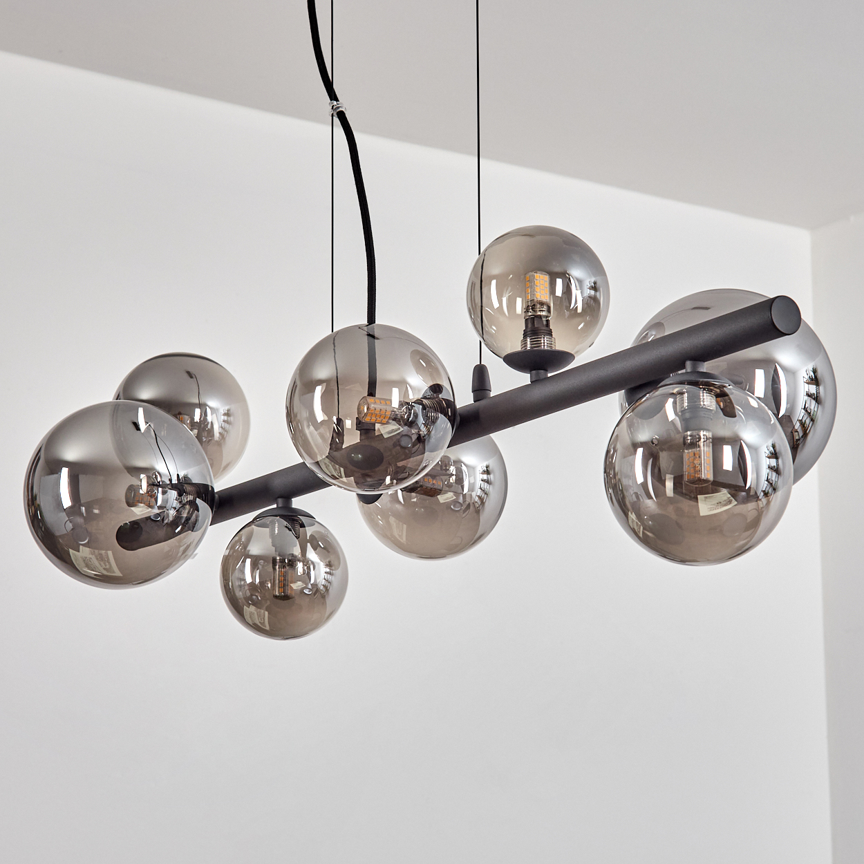 Eine moderne Hängelampe mit mehreren rauchigen Glaskugelschirmen und freiliegenden Glühbirnen hängt an einer weißen Wand.