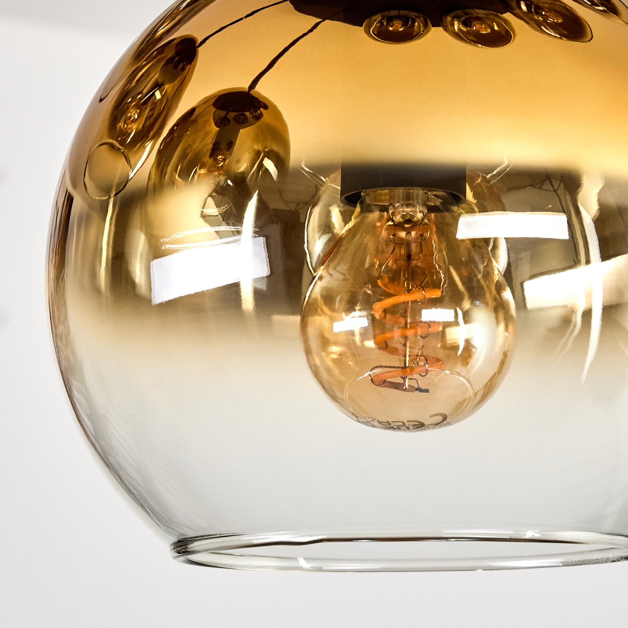 Nahaufnahme einer Glasleuchte mit einer Glühbirne im Inneren. Das Glas ist bernsteinfarben, der Hintergrund ist weiß.