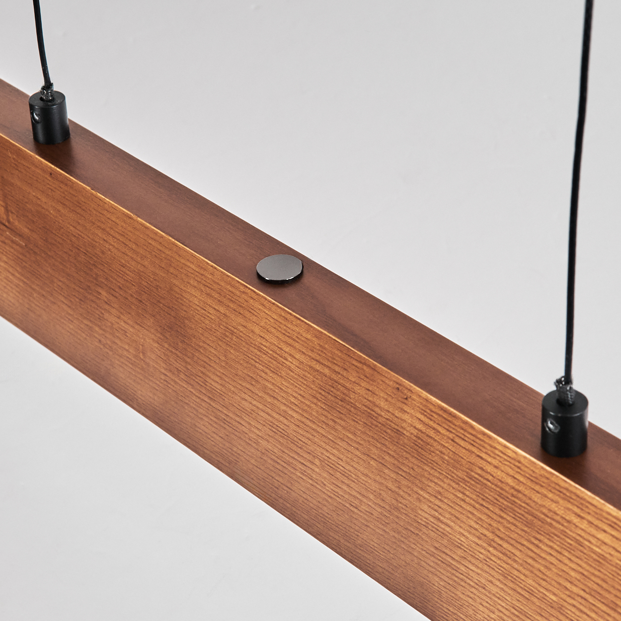 Nahaufnahme eines Holzbalkens mit dunklem Metallknopf. Schwarze Drähte mit schwarzen Steckern hängen vor weißem Hintergrund.
