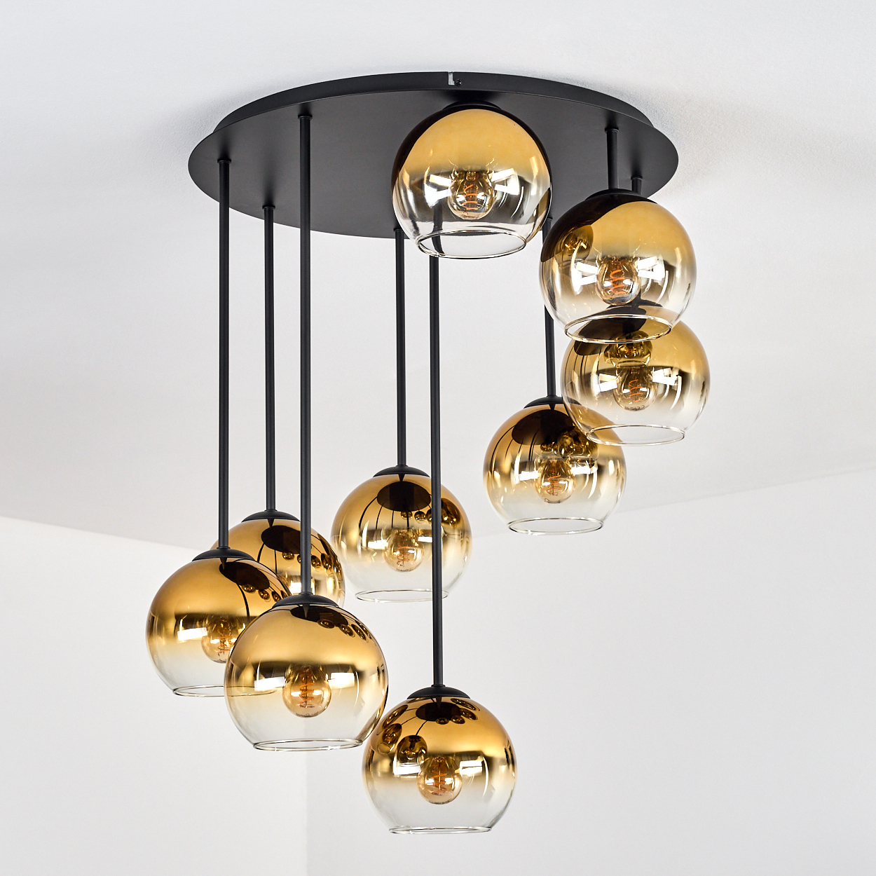 Ein moderner Kronleuchter mit acht goldenen Glaskugeln, die von einer schwarzen runden Basis an einer weißen Decke hängen.