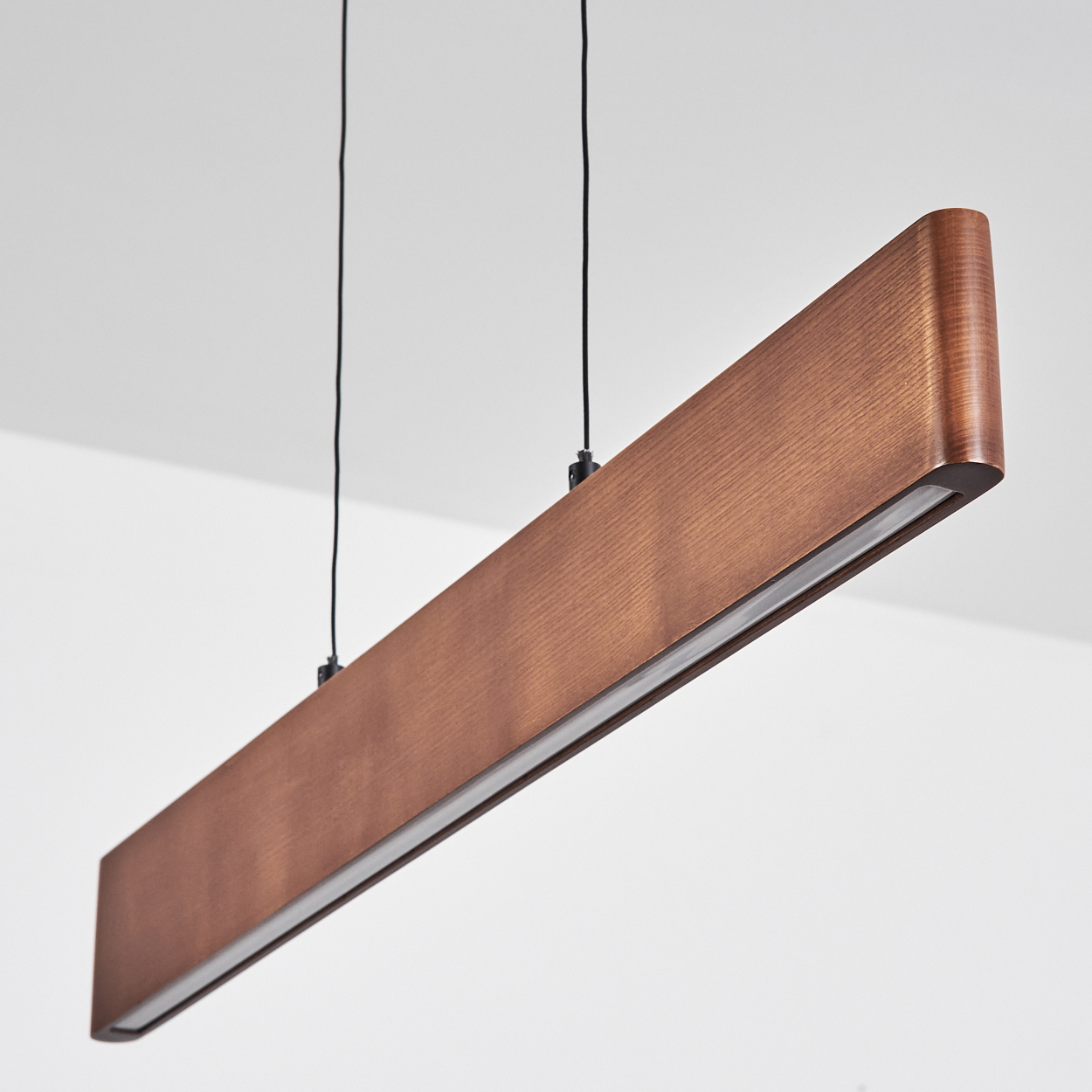 Eine rechteckige Pendelleuchte im Holzstil hängt von der Decke. Das Licht ist braun und hat eine weiße, lichtemittierende Platte unten.