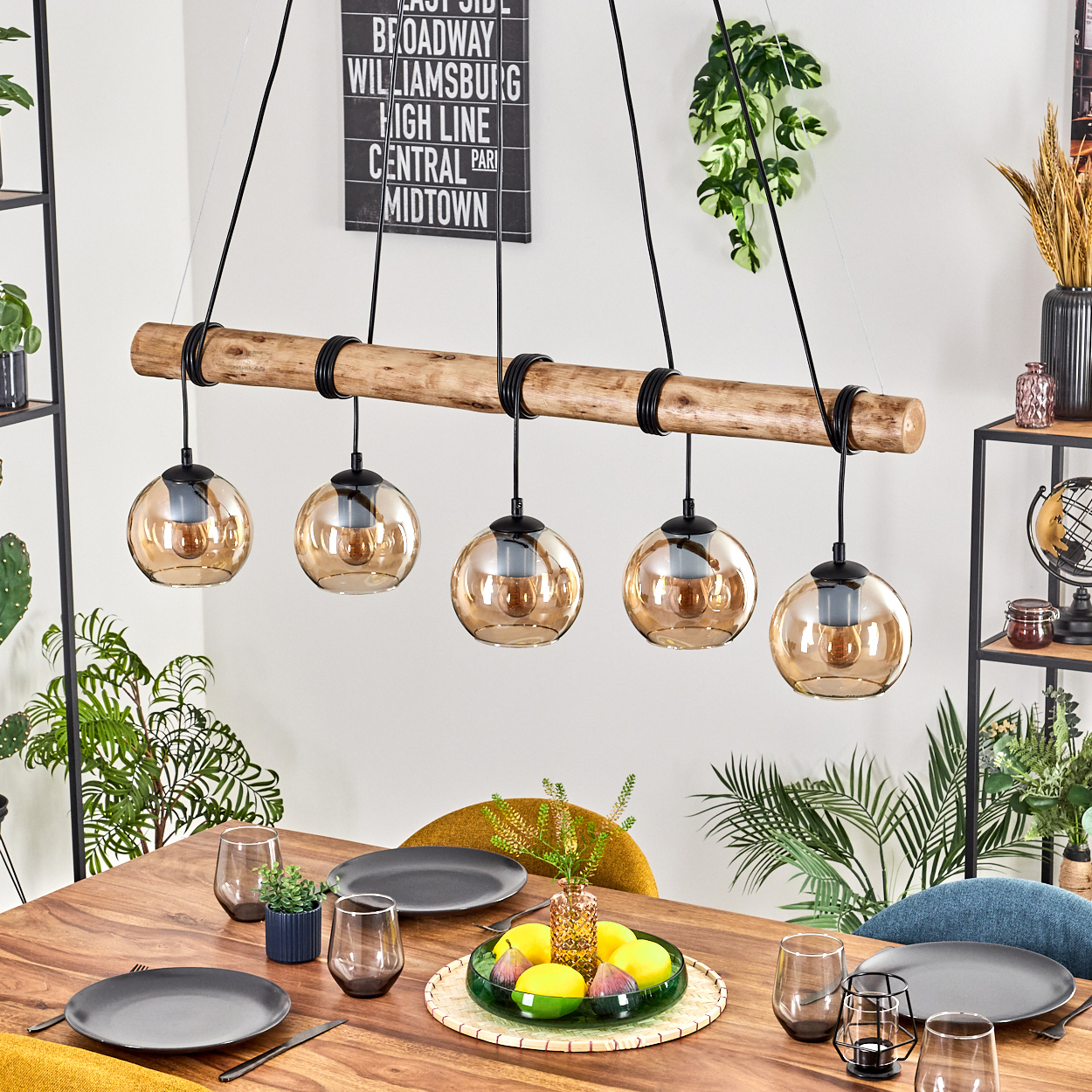 Ein Esstisch mit Tellern, Gläsern und einem Mittelstück. Darüber hängt ein Holzbalken mit fünf hängenden Kugellampen.