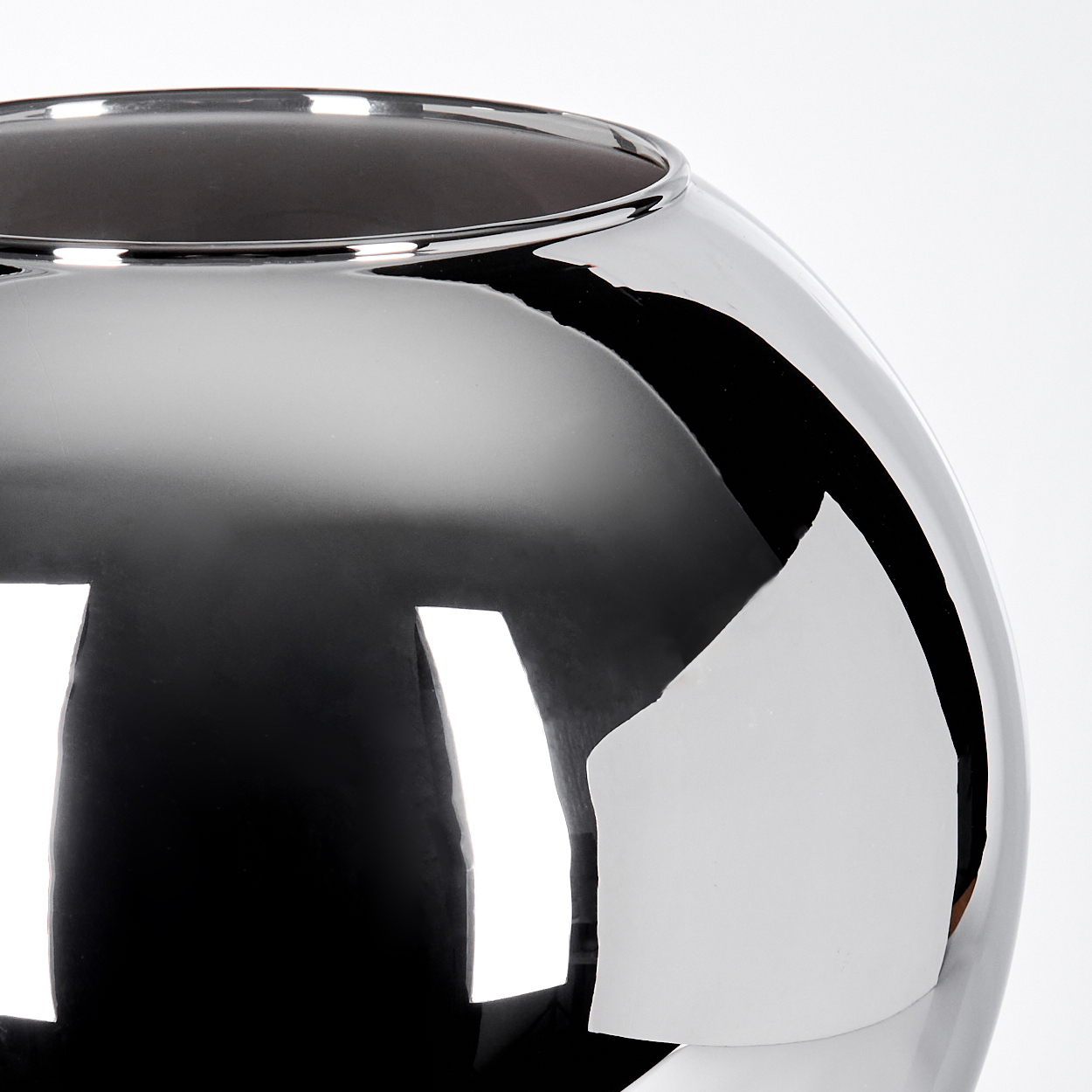 Nahaufnahme einer reflektierenden, silbernen kugelförmigen Vase. Die Vase hat ein dunkles Inneres und reflektiert helles Licht.