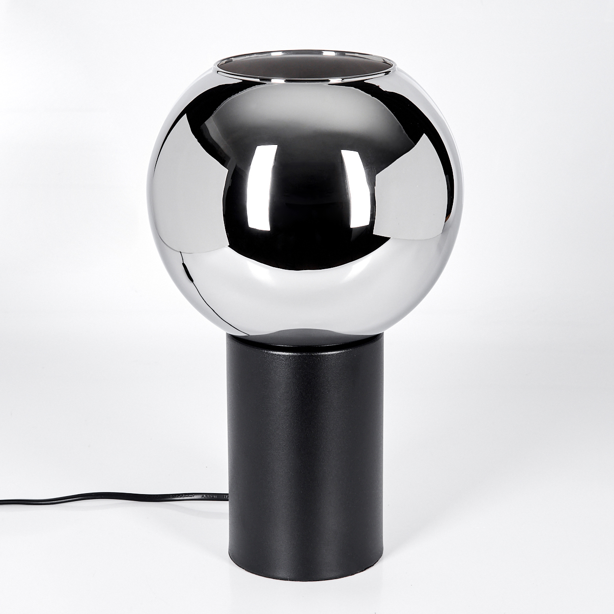 Eine moderne Lampe mit einer Chromkugel auf einem schwarzen zylindrischen Sockel. Ein schwarzes Kabel geht von der Basis aus.