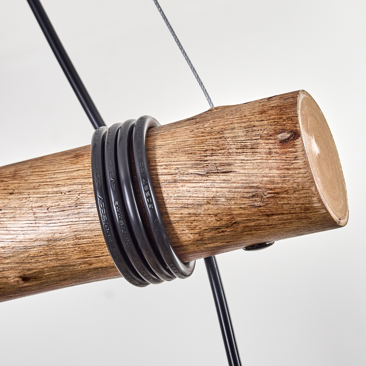Holzstamm mit schwarzen Drähten, die darum gewickelt sind, an einem Stahlseil vor weißem Hintergrund aufgehängt.