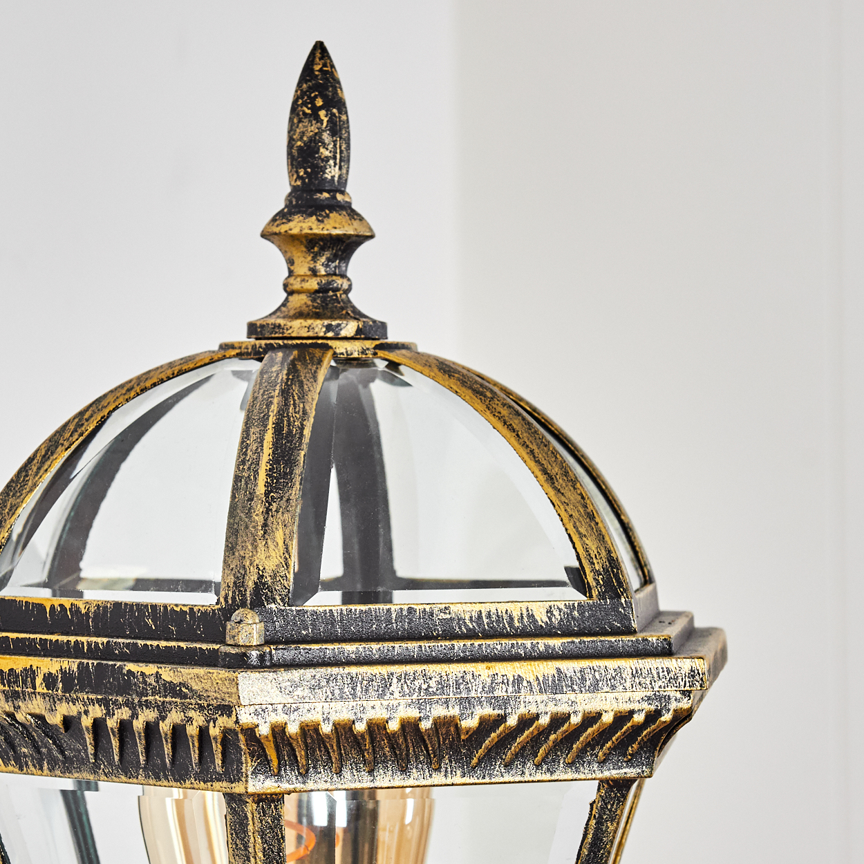 Nahaufnahme einer dekorativen Lampe. Sie hat eine gold-schwarze Oberfläche, Glasscheiben und eine spitze Spitze. Der Hintergrund ist weiß.
