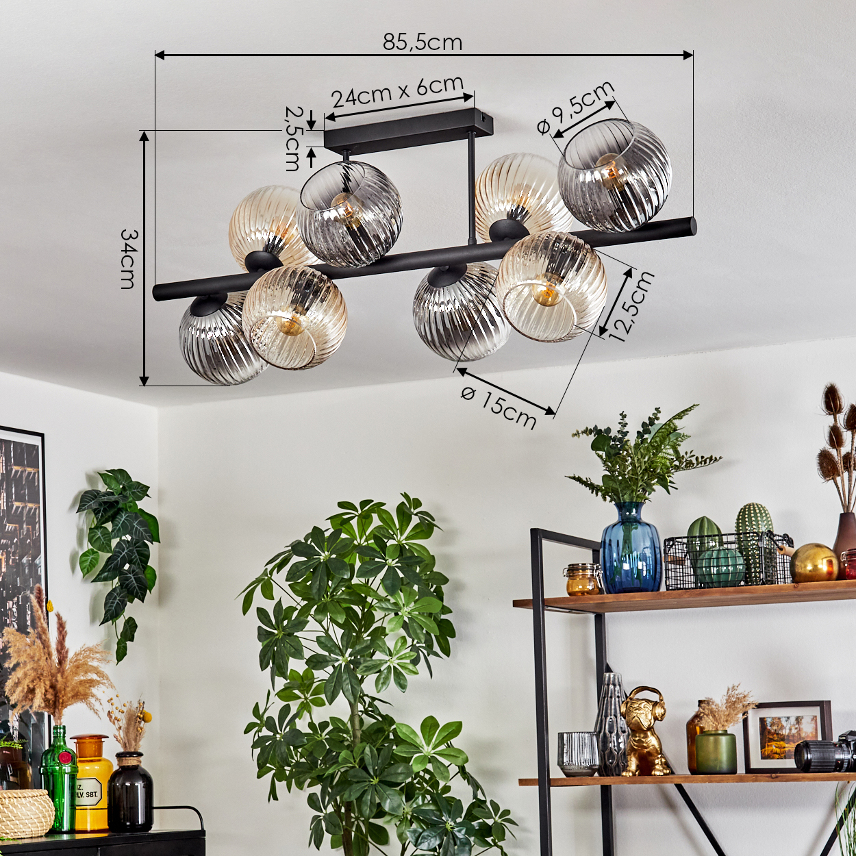 Eine moderne Deckenlampe mit Glaskugeln, Maße angegeben. Pflanzen und ein Regal mit Dekoration im Hintergrund.