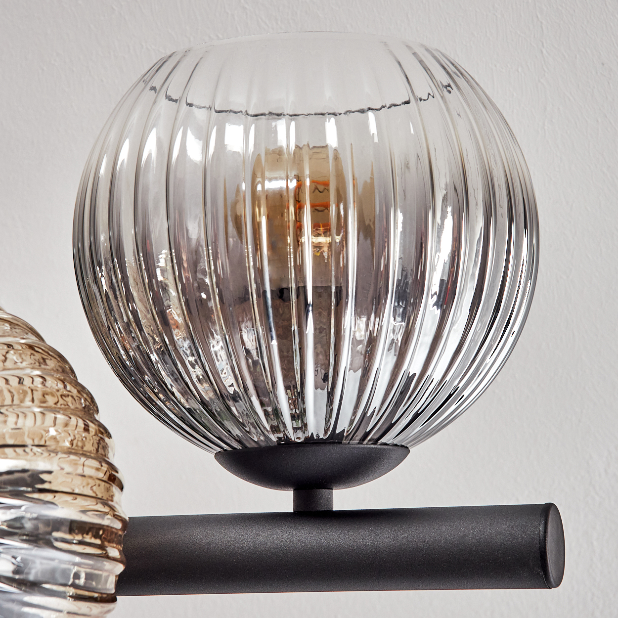 Nahaufnahme einer Glaslampe mit geripptem Design. Die Lampe hat eine Glühbirne und ist an einer schwarzen Metallstange befestigt.