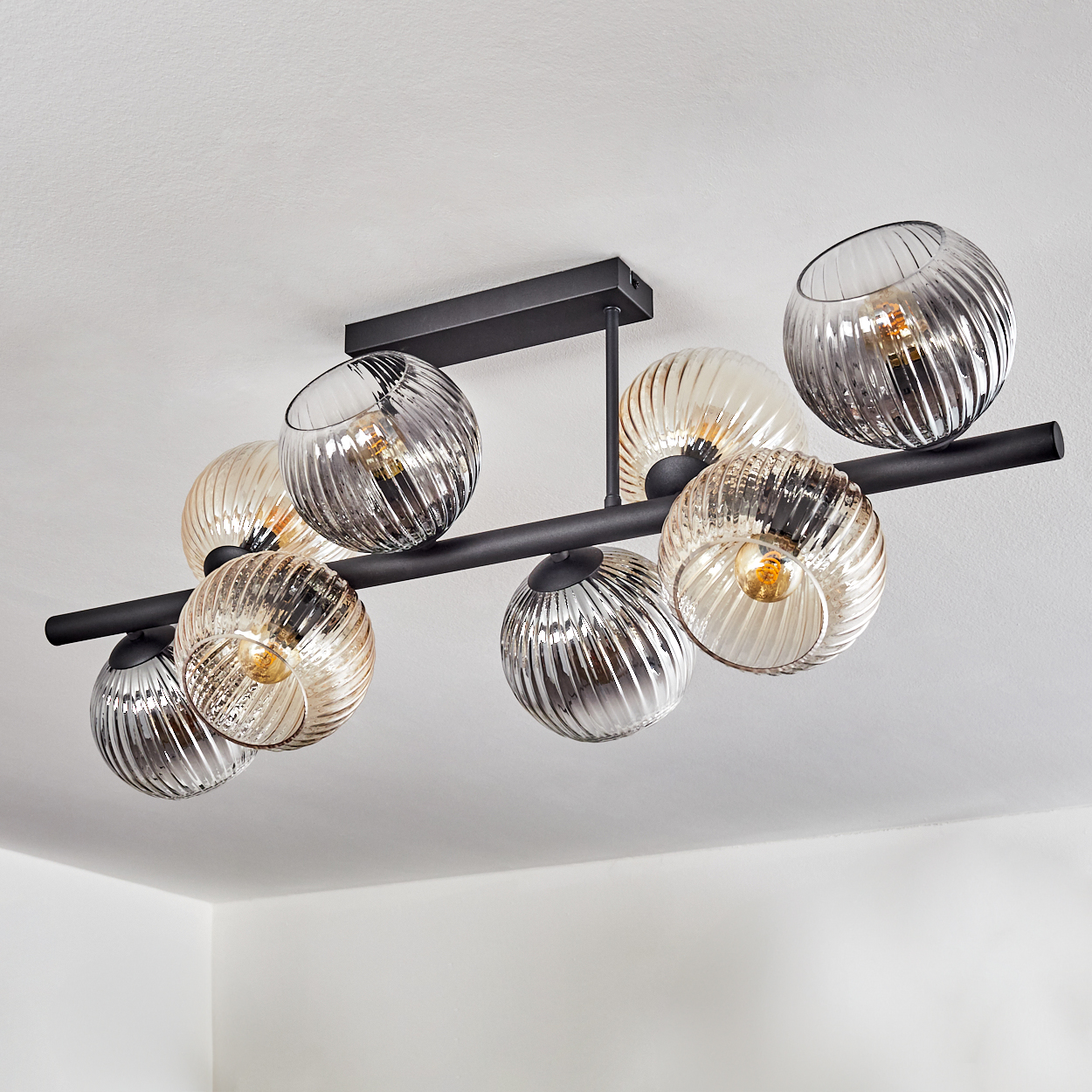 Eine moderne Deckenleuchte mit neun kugelförmigen, strukturierten Glasschirmen in Grau und Bernstein, befestigt an schwarzen Metallstangen.