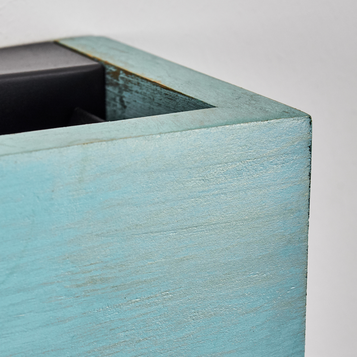 Nahaufnahme einer blau bemalten Holzkastenecke. Die Farbe ist abgenutzt, wodurch das Holz darunter sichtbar wird. Ein dunkler Innenraum ist sichtbar.