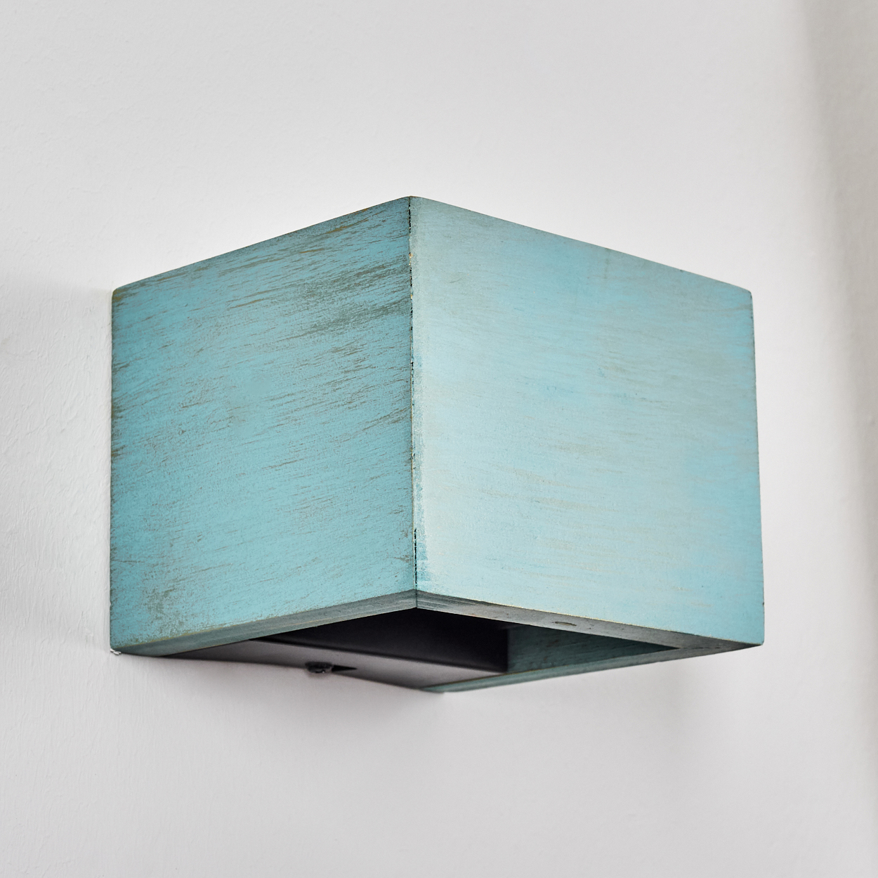 Ein quadratischer, hellblauer Holzkasten ist an einer weißen Wand befestigt. Die Box hat ein abgenutztes Finish und eine dunkle Unterseite.