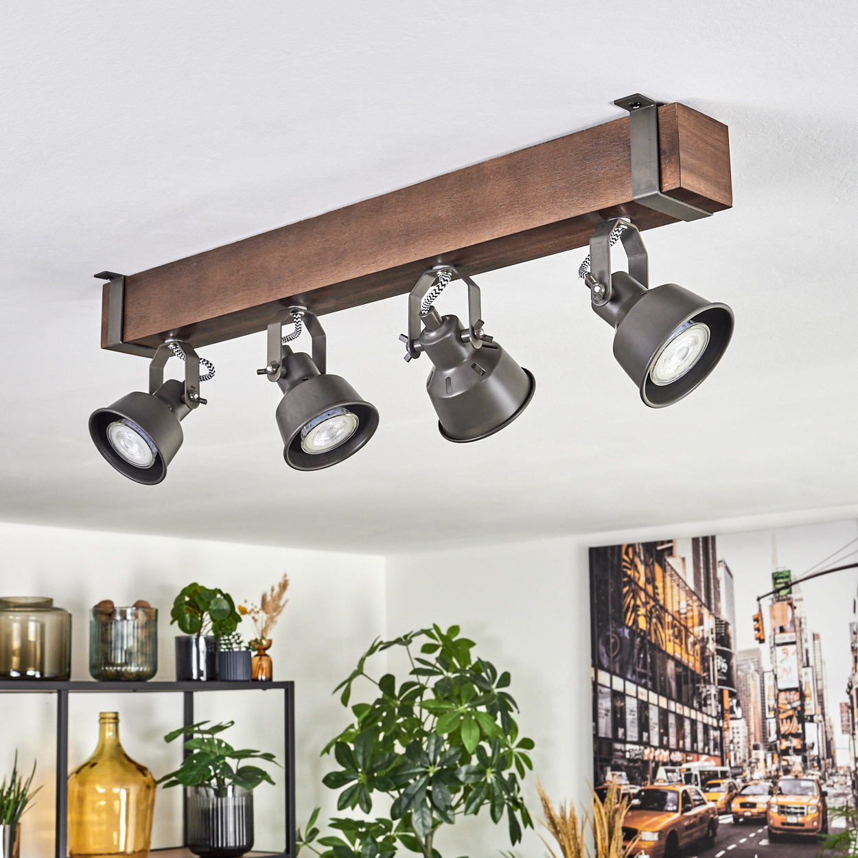 Deckenstrahler an einem Holzbalken. Schwarze Lampen, weiße Decke und ein Stadtbildgemälde sind im Hintergrund sichtbar.