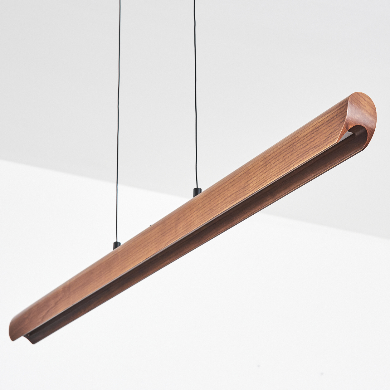 Eine rechteckige Holzleuchte hängt von der Decke. Sie ist braun und hat ein gebogenes Ende. Der Hintergrund ist weiß.
