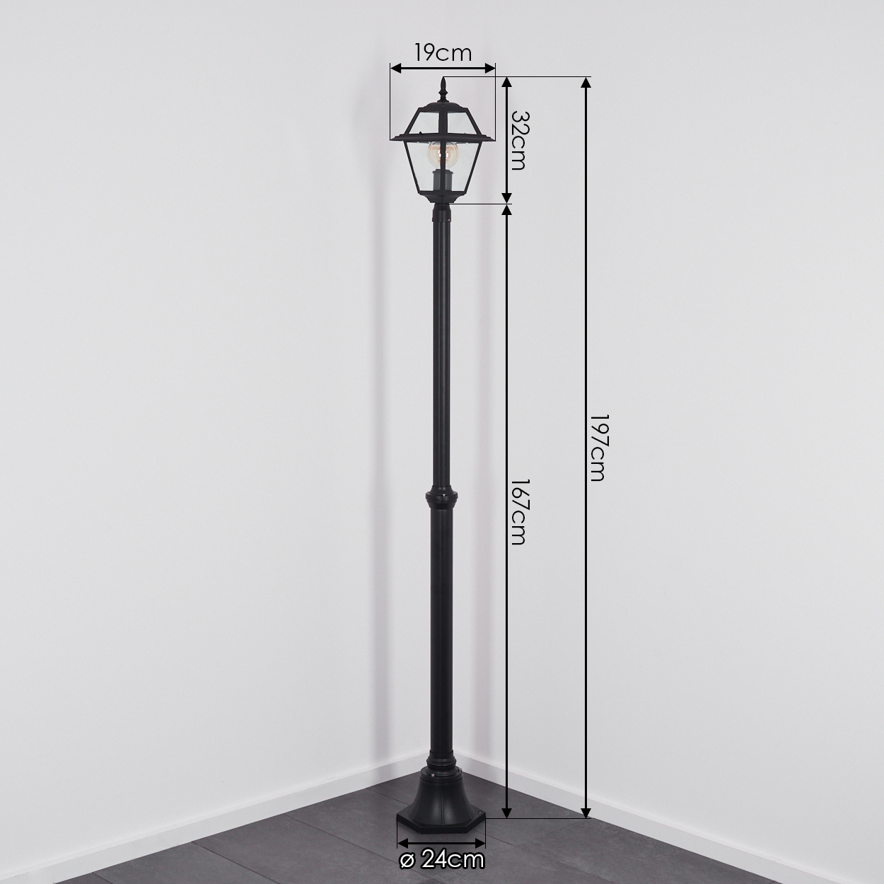 Schwarze Außenlampe. Maße: 19 cm breit, 32 cm hoch, 167 cm Stange, 197 cm Gesamthöhe, Sockel 24 cm. Es ist in einer Ecke.