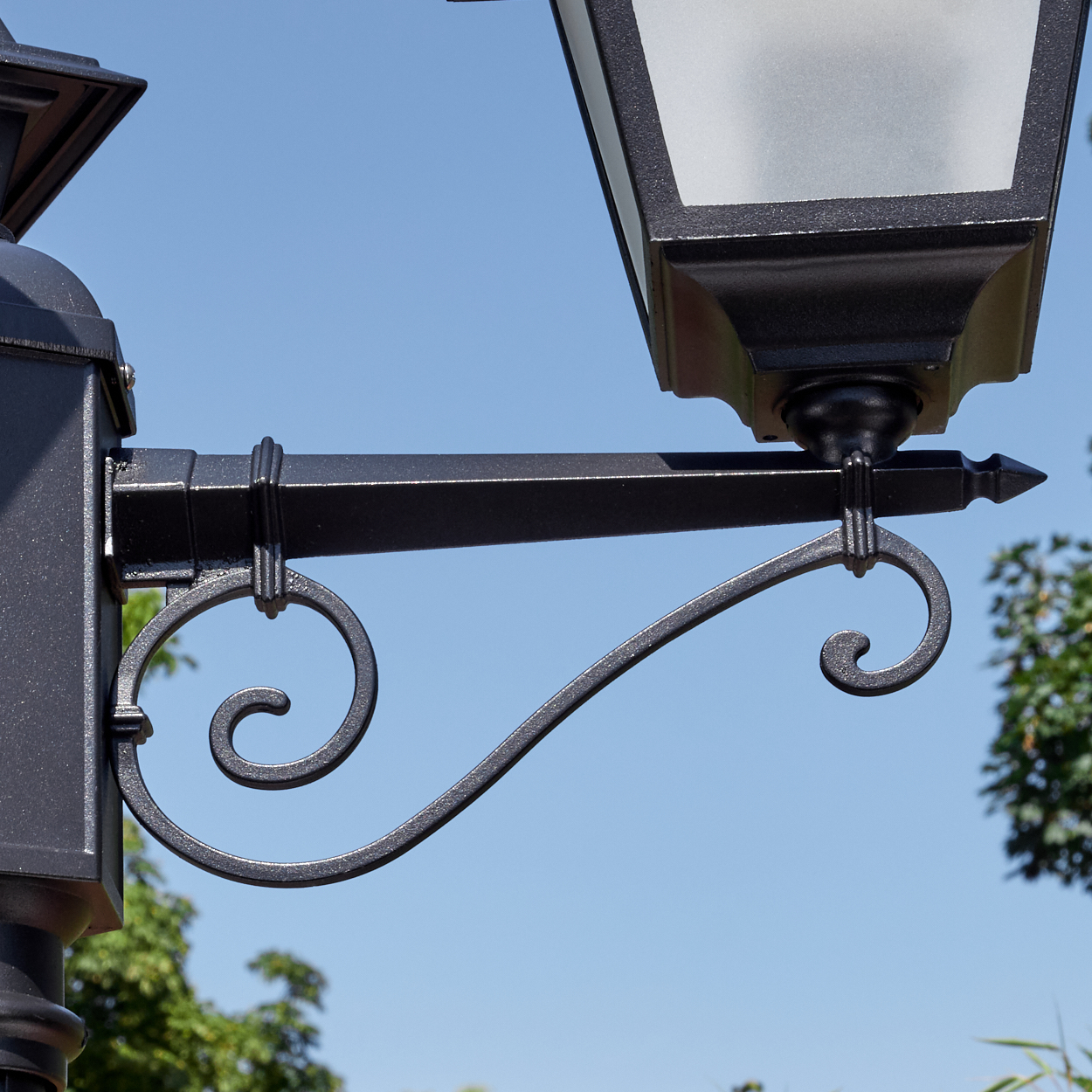 Nahaufnahme einer schwarzen, verzierten Straßenlaterne vor klarem blauem Himmel. Die Lampe hat dekorative Schnörkel und ein rechteckiges Licht.
