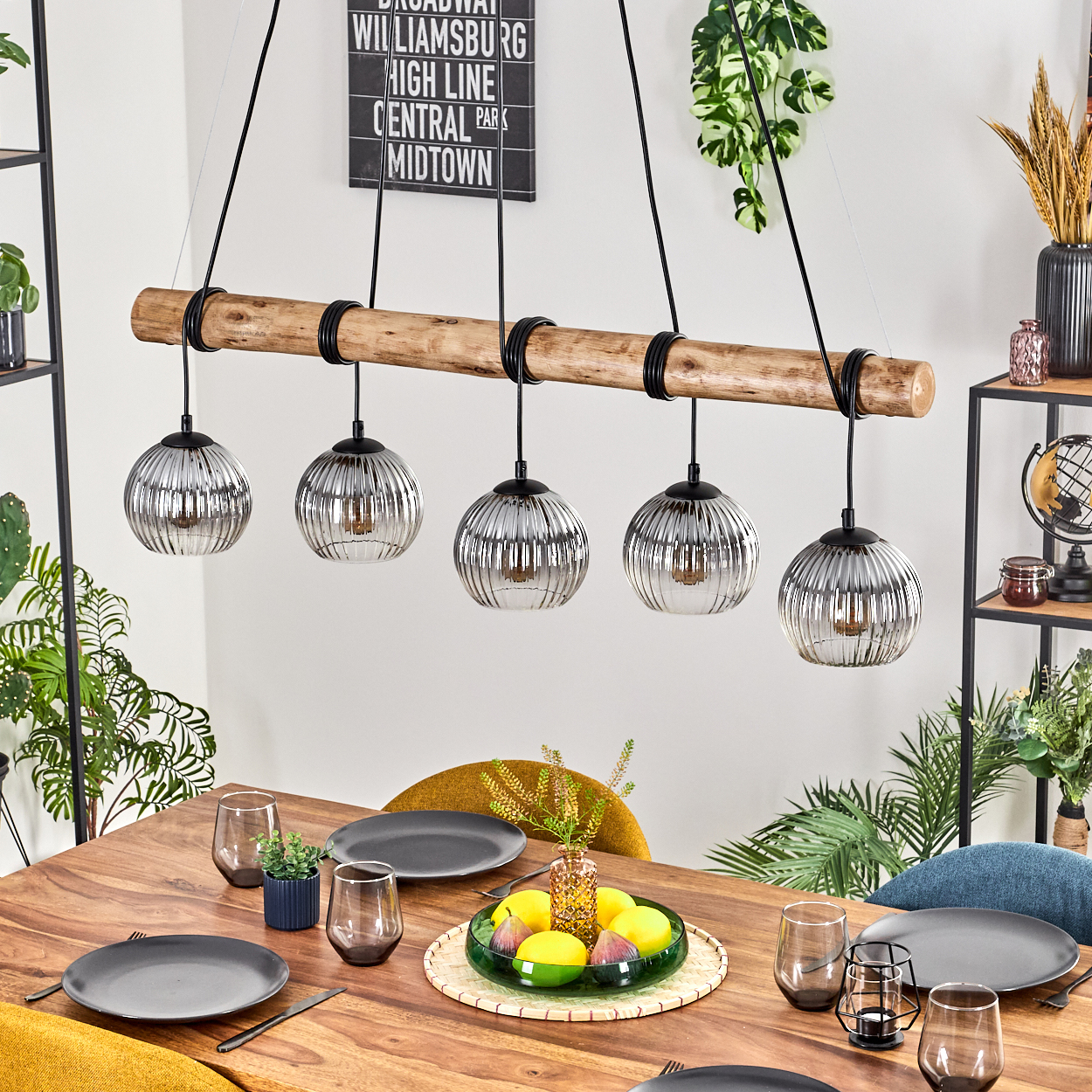 Esszimmer mit Holztisch, Hängelampen und Tischdeko mit Obst. Ein Schild hängt an der Wand.