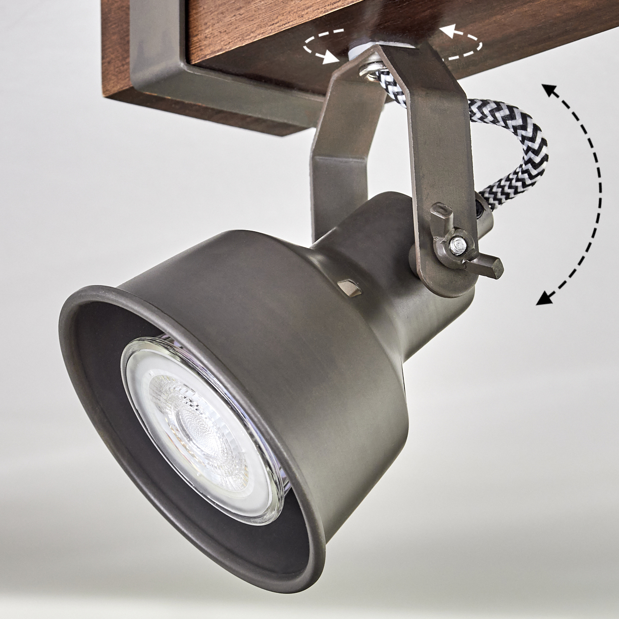 Ein dunkelgrauer Strahler ist auf einem Holzsockel montiert. Das Licht ist nach unten gerichtet. Ein schwarz-weißes Kabel ist sichtbar.